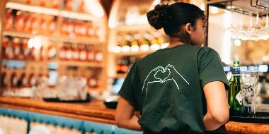 A waitress with her back to the camera stood in the bar area of the restaurant with her Ask Italian uniform on.